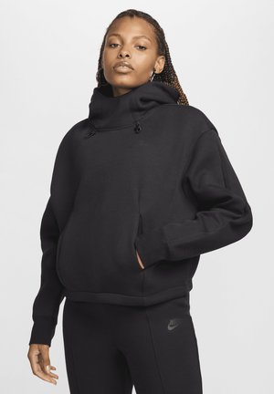 Sudadera negra con cuello alto, que cuenta con un bolsillo frontal, cordones y textura suave; combinada con pantalones negros a juego.