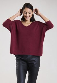 Burgunderfarbener, lässig geschnittener Pullover mit langen Ärmeln und V-Ausschnitt, kombiniert mit schwarzen, eng anliegenden Lederhosen. Weicher Stoff, lässiger Stil.