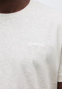 Κοντινό πλάνο ενός ανοιχτό γκρι T-shirt με στρογγυλή λαιμόκοψη και μικρό λευκό λογότυπο "BORG" στο αριστερό μέρος του στήθους.