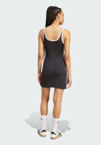 Čierne šaty bez rukávov s bielym lemom, priliehavý strih, dĺžka nad kolená, kombinované s bielymi ponožkami a topánkami so čiernymi pruhmi.