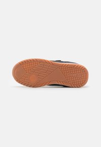 Semelle de chaussure de sport noire avec adhérence texturée, présentant une semelle extérieure en caoutchouc marron et des motifs pour traction et stabilité.