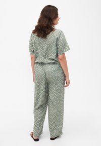 Zelený two-piece outfit s bodkami vyrobený z ľahkej tkaniny. Topy majú krátke rukávy a nohavice sú široké s elastickým pásom.