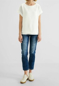 Vit texturerad t-shirt med kort ärm, blå tajta jeans och krämfärgade sneakers med bruna sulor. T-shirten har en avslappnad passform och rund halsringning.