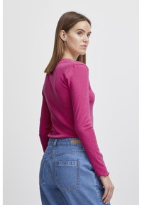Åtsittande långärmad topp i livfullt rosa ribbad material, i kombination med höga ljusblå jeans i denim med en läderlapp på baksidan.