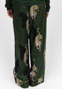 Groene broek met een gemengd patroon van leopards en zwarte panters, met een gladde textuur en een gouden accent langs de zoom.