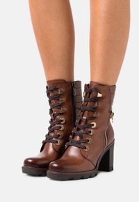 Bottines en cuir brun avec un laçage à l'avant, œillets en métal, fermeture éclair latérale, dos texturé et talon épais.