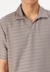 Camisa polo de manga curta em tecido canelado cinza claro com riscas horizontais, apresentando um colarinho clássico e uma abertura sem botões.