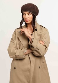 Bež trench coat lõdva lõikega, topeltkinnitatud nööbid ja laiad pöidlad; pruun villane barett nahkrihmaga.