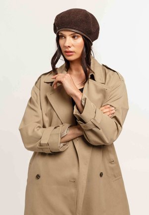Trench coat beige con una vestibilità rilassata, bottoni doppi, e maniche larghe; berretto di lana marrone con una banda di pelle.