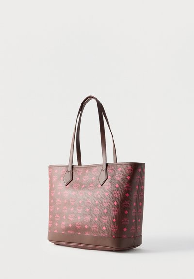 Sac cabas marron avec motif logo MCM rose et deux longues anses, debout sur fond blanc.