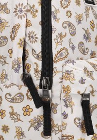 Witte stoffen rugzak met een bloemen-paisleypatroon in geel, blauw en groen. Zwarte ritsen en accenten met zichtbare merkhardware.