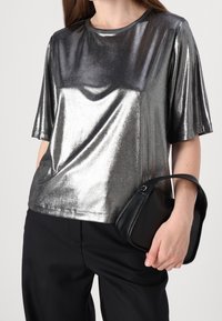 Camicia corta in tessuto metallico argento con una texture liscia, scollo rotondo e design drappeggiato. Abbina una borsa nera.