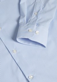 Chemise à manches longues rayée bleu clair et blanc, avec poignets boutonnés et boutons blancs sur le devant.