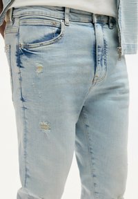 Světle modré džínové kalhoty s výraznými detaily, jako jsou roztrhání a malé díry, pět kapes a jemné vyblednutí na látce.