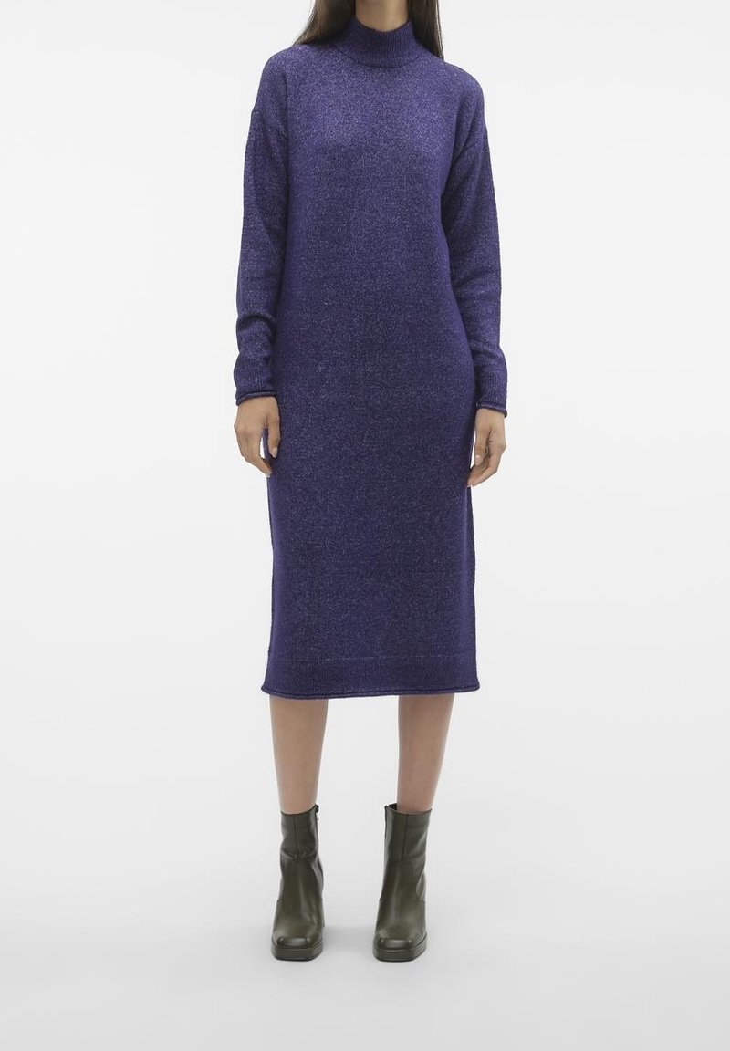 Vestito a maglia viola con colletto alto, maniche lunghe e lunghezza fino al polpaccio. Il tessuto ha una texture sottile. Abbinato a stivali alla caviglia verde scuro.
