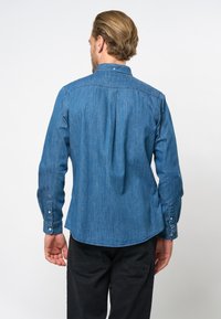Denim overhemd in medium blauw, met een rugplooi, lange mouwen met knoopmanchetten en een afgeronde zoom. Draag het met zwarte broek.