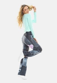 Hellblaues Langarmoberteil kombiniert mit dunkelblauen Jeans mit Patchwork-Design, abgenutzten Details und einem rosa Herzakzent. Weiße Sneaker.
