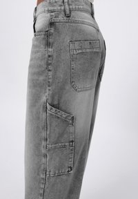 Pantalones cargo en denim gris con un corte relajado, bolsillos laterales y bolsillos traseros de parche. Textura suave con áreas desgastadas para un interés visual.