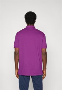 Paarse polo shirt met korte mouwen gezien vanaf de achterkant, met een klassieke kraag en een rechte zoom, gemaakt van een gladde stof.