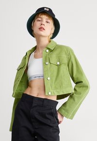 Veste en velours côtelé écourtée de couleur vert vif avec des boutons en argent, comportant deux poches poitrine et un col, associée à un pantalon noir.