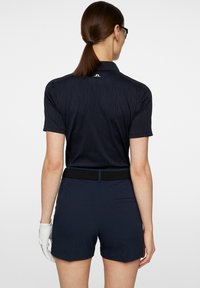 Marinblå pikétröja med strukturerat mönster, korta ärmar och krage; kombinerad med marinblå shorts och svart nätbälte. Vit handske på vänster hand.