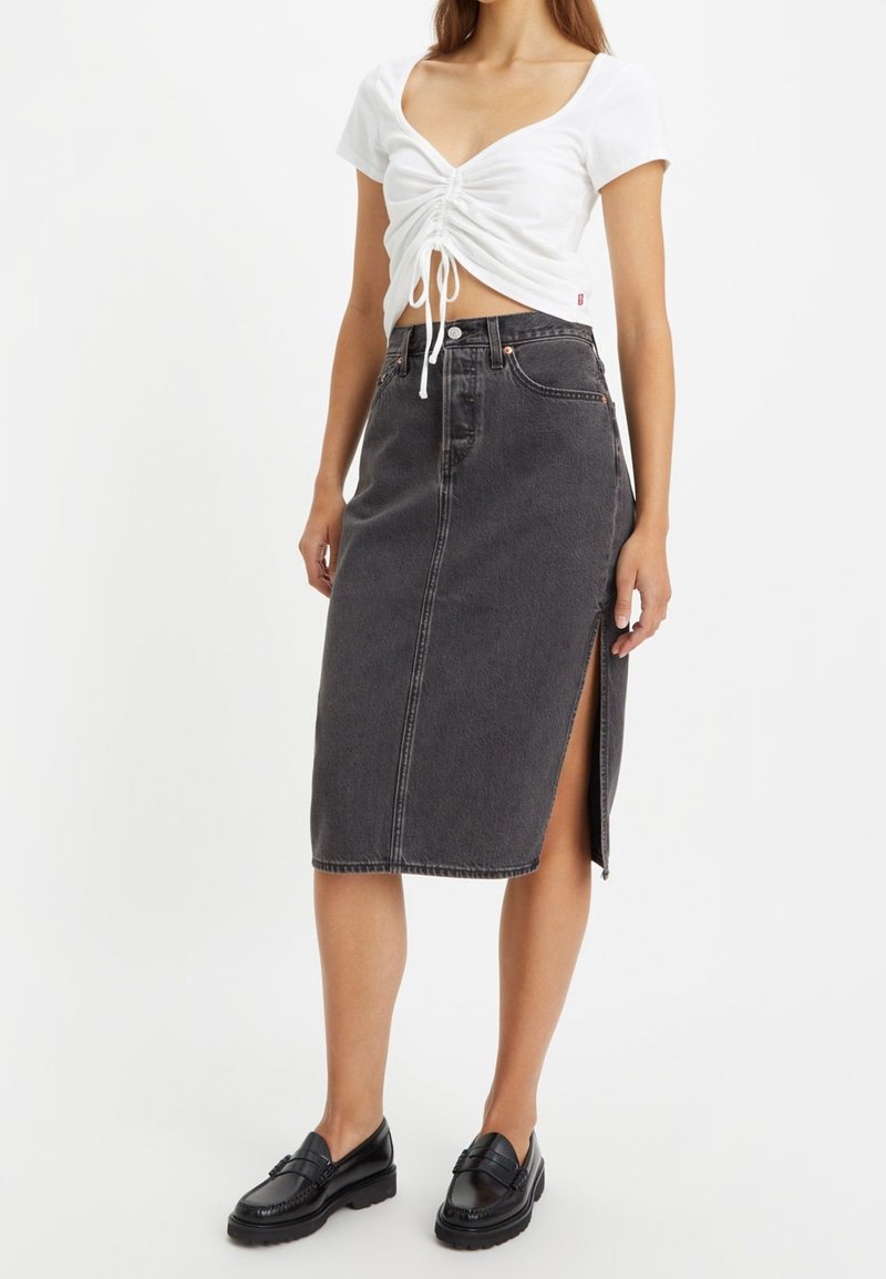 Musta denim midi-hame suoralinjaisella leikkauksella, sivuhalkiolla ja näkyvillä saumoilla. Yhdistetty valkoiseen istuvaan toppiin ja mustiin loafereihin.