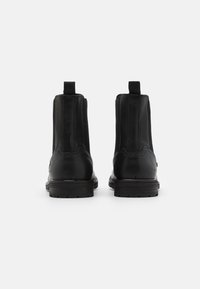 Bottes Chelsea en cuir noir au toucher lisse, avec panneaux élastiques sur les côtés et languette d'extraction à l'arrière. Semelle en caoutchouc noire robuste avec crampons.