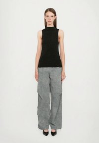 Črna brezrokavna majica iz teksturirane tkanine, kombinirana z ohlapnimi sivimi cargo hlačami z žepi spredaj in ravnim krojem hlačnic, nošena s črnimi petami.