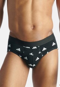 Mustat alushousut, joissa on graafinen kuvio valkoisista kolmioista, joustava vyötärö ja tiukka istuvuus. Valmistettu sileästä kankaasta, jossa on mattapinta.