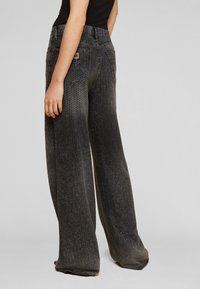 Fekete, széles szárú farmernadrág texturált anyagból, melyet fém szegecsek díszítenek, magasított derékkal és hátul zsebekkel a funkcionalitás érdekében.