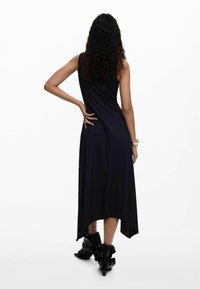 Czarna, bezrękawnikowa sukienka z asymetrycznym dołem i gładką, miękką teksturą. Noszona z błyszczącymi czarnymi botkami za kostkę.