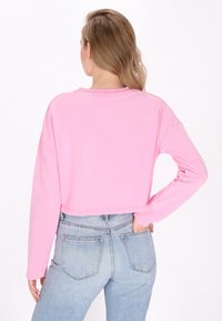 Top corto de manga larga en tejido de color rosa claro con cuello redondo y ajuste holgado. Combinado con jeans de tiro alto en tono azul claro.