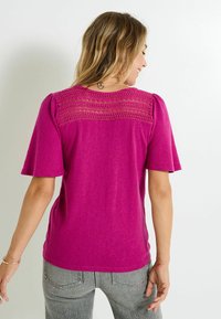 Camiseta de punto fucsia con mangas cortas, que presenta un panel de encaje texturizado en la parte trasera y un corte relajado. Material suave y ligero.
