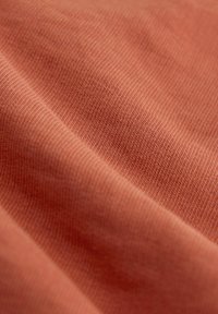 Rosa geripptes Material mit glatter Textur, das eine Nahaufnahme feiner Nähte und Falten zeigt und damit die weichen und flexiblen Eigenschaften betont.