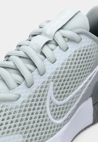 Close-up of light gray Nike sneaker with mesh upper, thick laces, and white swoosh logo on the side.