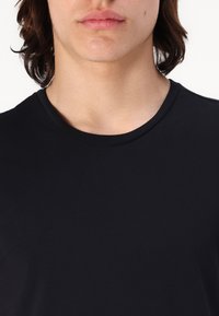 T-shirt noir à col rond, fabriqué en tissu doux. Présente une texture lisse et un design ajusté, idéal pour un usage décontracté.