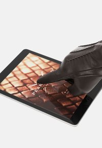 Ein brauner Ledergstock, der auf einem Tablet-Bildschirm drückt, der einen strukturierten Hintergrund in warmen Tönen mit einem Logo und digitalen Interface-Elementen anzeigt.