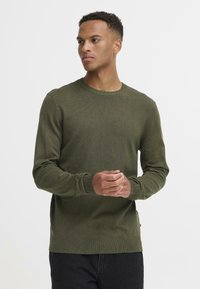 Olivengrønn strikkegenser med rund halslinning, lange ermer og ribbestrikket mansjetter og nederkant. Har en jevn tekstur og tettsittende design.