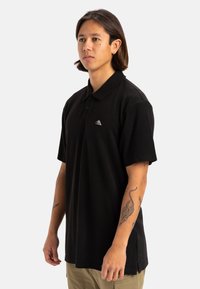 Polo nero in cotone, con colletto, maniche corte e un piccolo logo ricamato sul lato sinistro del petto.