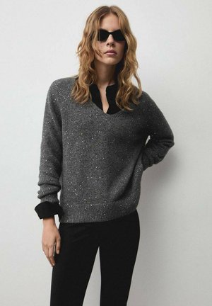 Grauer Strickpullover mit silbernen Sprenkeln, V-Ausschnitt und schwarzen Bündchen, kombiniert mit schwarzen Hosen. Hat eine lockere Passform und eine weiche Textur.