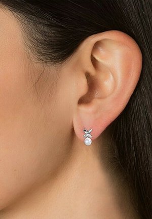 Orecchini a perno in argento con design a croce, completi di una piccola goccia di perla. Le texture opache e lucide contrastano con una finitura liscia.