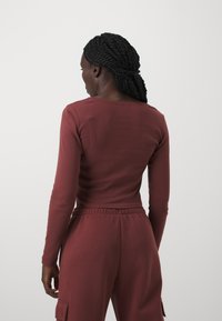 Burgundy színű, hosszú ujjú felső, puha anyagból; testhezálló fazon, kerek nyakkivágással. Hozzá illő, elasztikus derékkal ellátott jogger nadrággal párosítva.