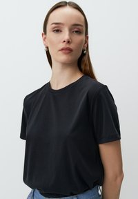Czarny T-shirt z krótkim rękawem wykonany z miękkiej bawełny. Posiada okrągły dekolt i luźny krój, bez widocznych wzorów czy ozdób.