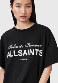 T-shirt nera oversize in cotone con testo bianco: "Infinite Summer ALLSAINTS LONDON." Collo rotondo, maniche corte, texture liscia.