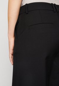 Czarne dopasowane spodnie z gładką teksturą, prostym krojem, szlufkami na pasek i subtelnym detalem tylnej kieszeni.