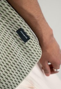 Green knit fabric featuring a geometric pattern in darker shades, with a black label reading "PROHIBITED" attached at the edge.