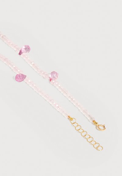 Deux bracelets délicats en perles roses avec des pierres roses en forme de goutte et des fermoirs en chaîne dorée sur un fond clair.