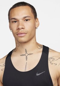 Schwarzes sportliches Tanktop mit rundem Ausschnitt und dünnen Trägern. Verfügt über ein kleines graues Nike-Logo auf der Brust und sichtbare Tattoos am Hals.