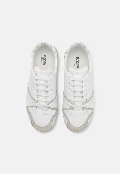 Zapatillas blancas de cuero con detalles de ante gris. Tienen puntera redonda, cordones en la parte delantera y un logo en la lengüeta. Textura suave, diseño clásico.