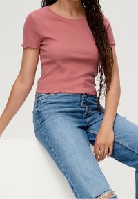 Kortærmet, tætsiddende, ribbet T-shirt i støvet rosa med bølget kant; parret med lyseblå, højtaljede, slidte jeans.